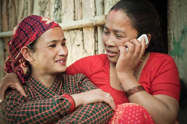 Two mature, Nepalese women talking on phone happily.