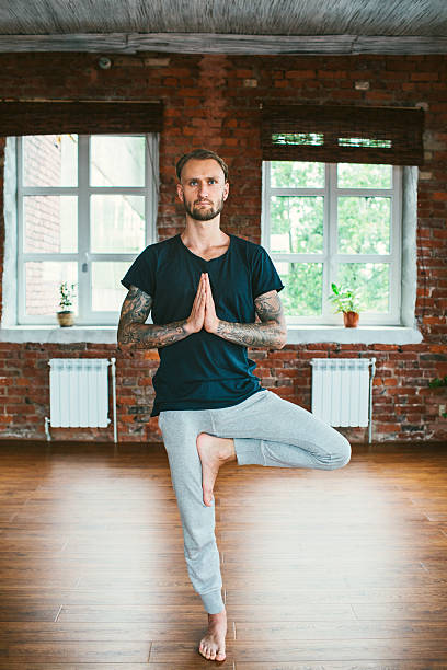 Man doing yoga in studio Young Caucasian man doing yoga in studio man yoga tattoo stock pictures, royalty-free photos & images