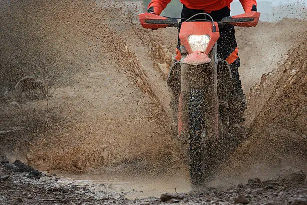 Motocross driver splashing mud on wet and muddy terrain