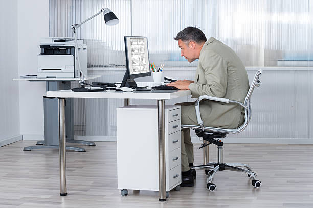 Concentrated Businessman Using Computer At Desk Side view of concentrated businessman using computer at desk in office bad posture stock pictures, royalty-free photos & images