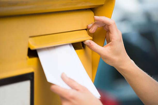 woman's hands inserting letter in mailbox - correspondência imagens e fotografias de stock