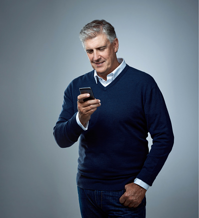 Studio shot of a mature man using a phone against a gray background