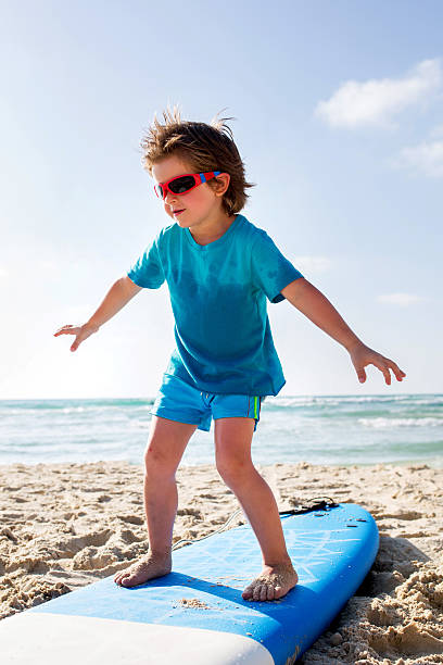 istock Small boy balancing on surfboard on the sand. 609698696