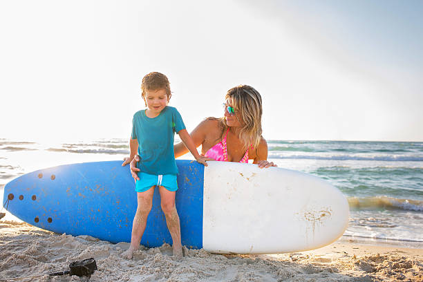 istock Mother and son with surfboard at the beach. 609698796