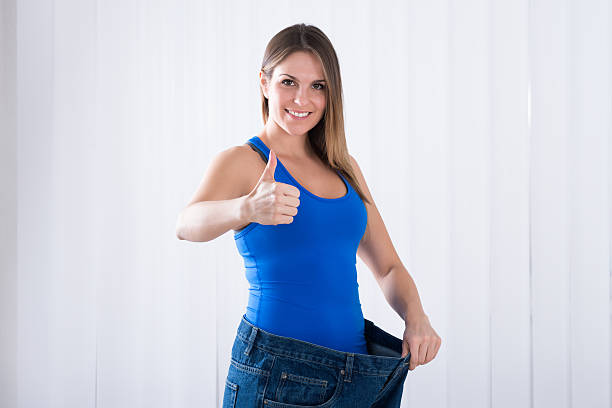 mujer mostrando su pérdida de peso usando pantalones vaqueros - loose weight fotografías e imágenes de stock