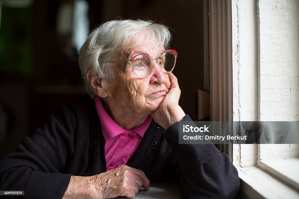 Elderly woman in glasses thoughtfully looking out the window. Senior Adult Stock Photo