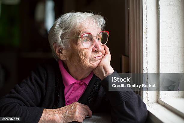 Elderly Woman In Glasses Thoughtfully Looking Out The Window Stock Photo - Download Image Now