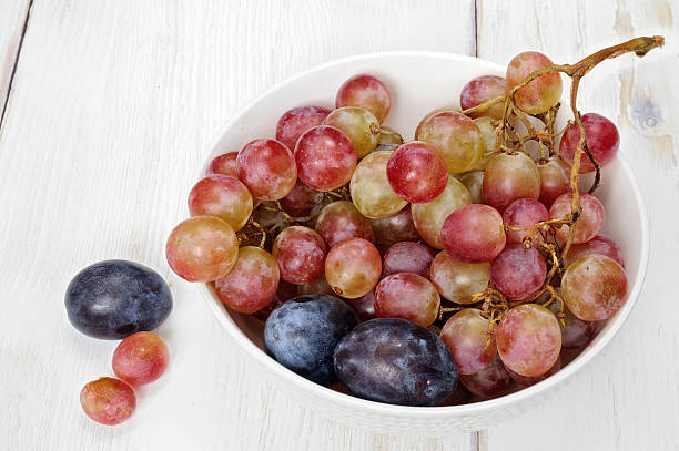 istock Plums and grapes in bowl on the white wooden table 609713668