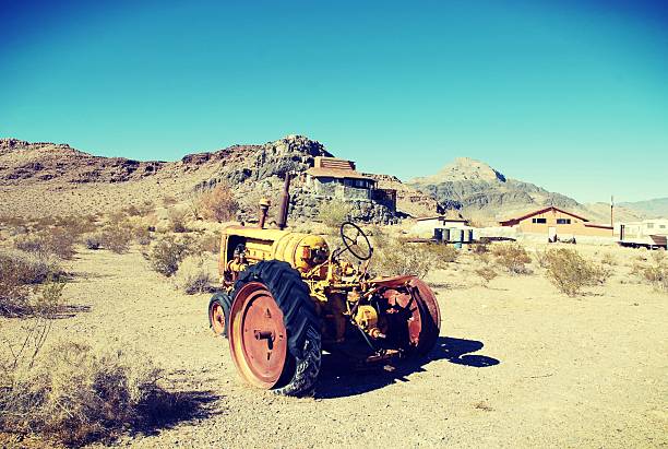 Yellow tractor in the middle of the Death Valley desert with some houses around. With a blue sky and a dry soil.