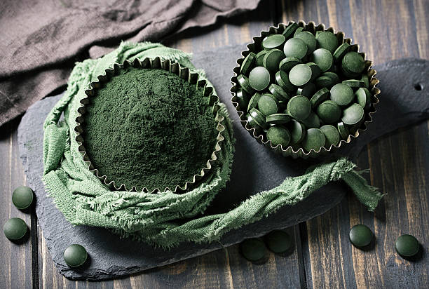 Spirulina tablets and powder in bowls Spirulina tablets and powder in bowls on a wooden background chlorella stock pictures, royalty-free photos & images