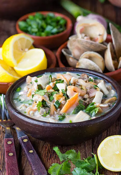 Latin American food. Seafood shellfish ceviche raw cold soup salad of seafood shellfish almejas, lemon, cilantro onion in clay bowl on wooden background. Traditional dish of Peru or Chile
