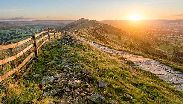Stone Footpath Along Mountain Ridge In Peak District. A stone footpath and wooden fence leading a long The Great Ridge in the English Peak District. Taken at sunrise, the image features beautiful Autumn vibrant colours from the rising sun. peak district national park photos stock pictures, royalty-free photos & images