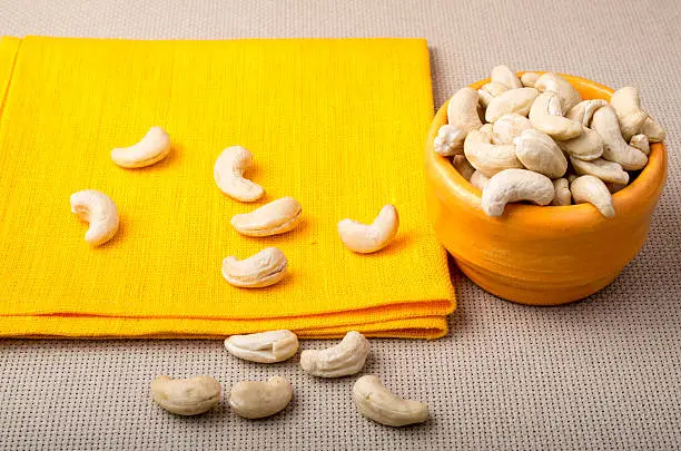 Selective focus on the tablecloth and raw cashew nuts in a small orange cup on orange napkin closeup
