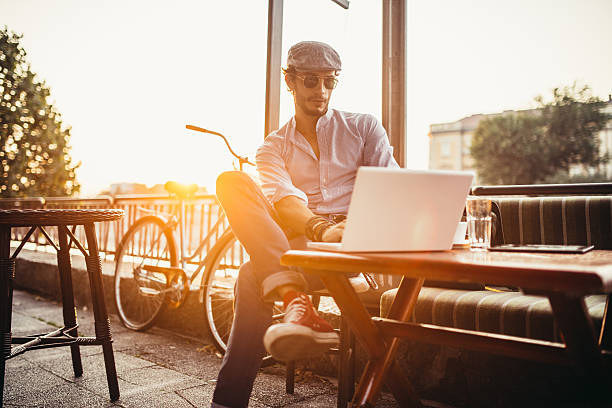 Hipster in cafe on laptop Handsome young hipster sitting in a cafe and working on laptop hipster bike stock pictures, royalty-free photos & images