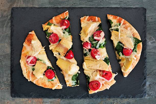 Flatbread pizza with mozzarella, tomatoes, spinach and artichokes on slate Flat bread pizza with melted mozzarella, tomatoes, spinach and artichokes, overhead view on slate flatbread stock pictures, royalty-free photos & images