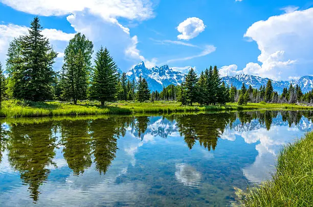 A panoramic spring view of clear and calm Snake River flowing at base of Teton Range in Grand Teton National Park, Wyoming, USA. 