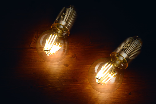Two LED filament classic styled bulbs on wooden board background.