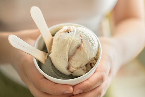 Regional Food Elements:  Closeup of organic, non-dairy, nut free, vegan ice cream held by a young woman.  Made with coconut and sweet potato.  Vanilla chocolate swirl and fennel licorice flavours, with 2 wooden spoons.  Vancouver, British Columbia, Canada.