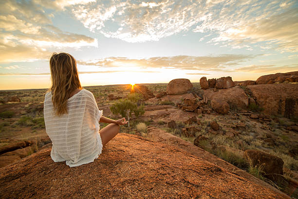 日の出にヨガをする白人女性 - devils marbles ストックフォトと画像