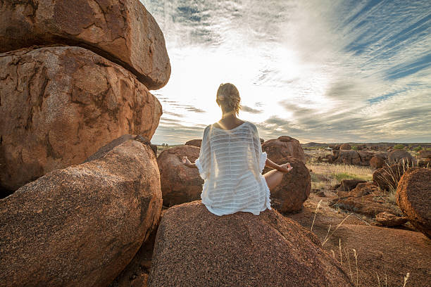 Female on boulder exercises yoga at sunset