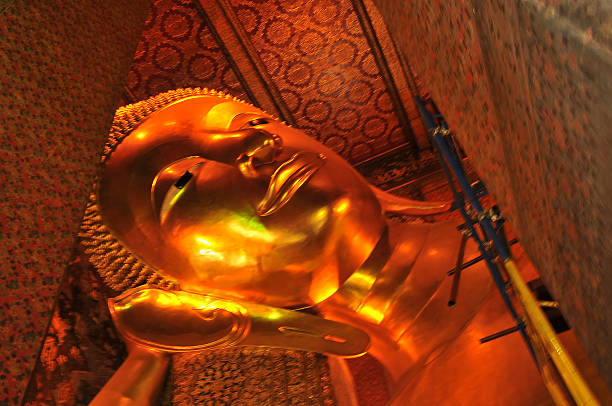 Bangkok, Thailand - February 18, 2013: Tourists are standing in front of huge reclining and sleeping buddha in Wat Pho, famous landmark and enormouss tall buddha about 44 meter length. People are taking photos. View from feet til head.