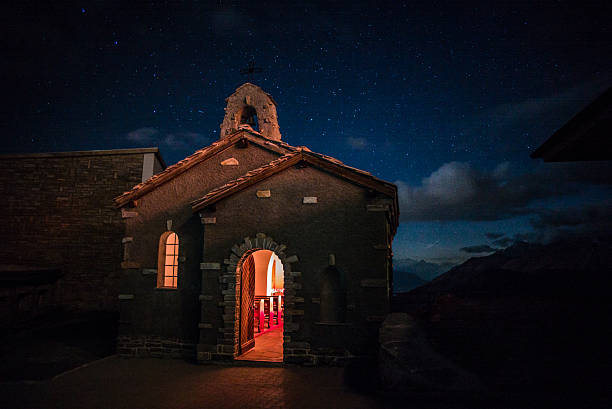 The warm glow of candlelight comes from a chapel in the swiss alps at night under the stars.