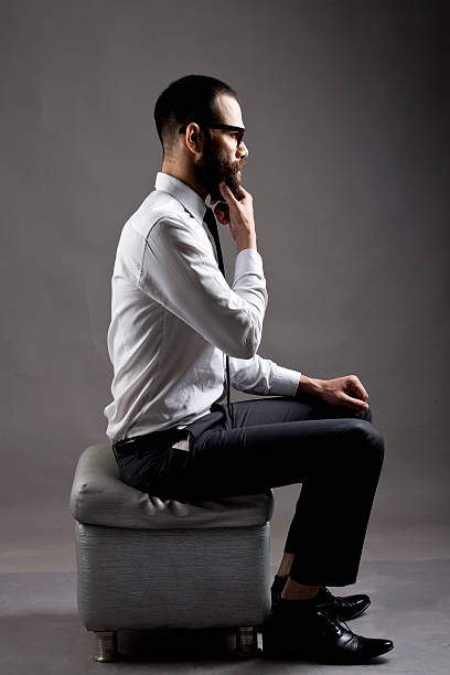 Side profile view of thoughtful young businessman wearing formalwear and sitting on ottoman.
