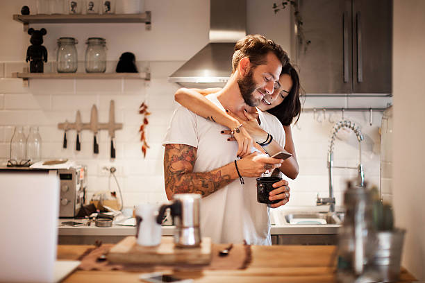 jeune couple à la maison utilisant un smartphone - heure du petit déjeuner du matin - maison témoin maison photos et images de collection