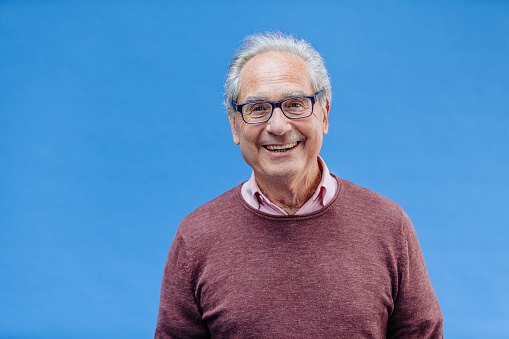 Portrait of a natural smiling, happy senior French businessman with glasses and smart casual, real people studio shot with copy space on blue background. XXXL