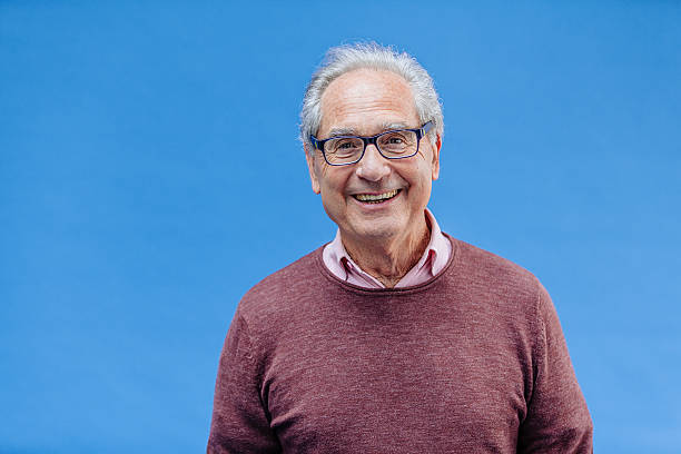 Portrait of a Smiling Senior Business Man Portrait of a natural smiling, happy senior French businessman with glasses and smart casual, real people studio shot with copy space on blue background. XXXL multi coloured glasses stock pictures, royalty-free photos & images