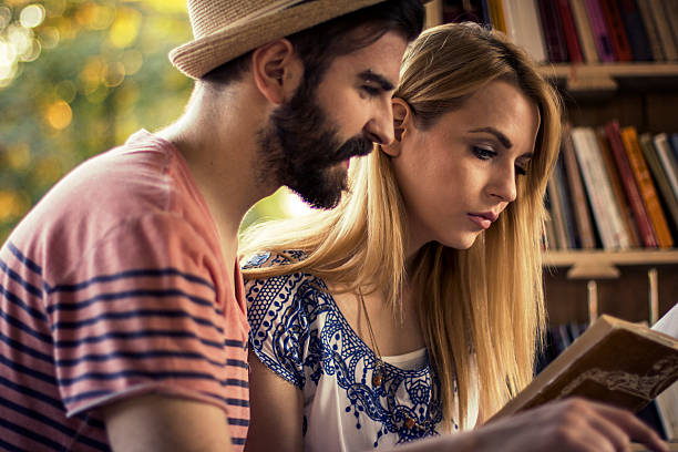 istock Young and happy couple reading same book in nature 609912490
