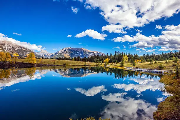 The concept of recreational tourism. Bright shining autumn day in Canmore, near Banff National Park. Majestic mountains and scenic cumulus clouds are reflected in the lake