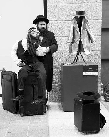 Jerusalem, Israel - February 19, 2014: Unidentified Jewish ultra-orthodox man performing with his puppet depicting orthodox Jew at Mamilla promenade. Selective focus on the hat for the coins.