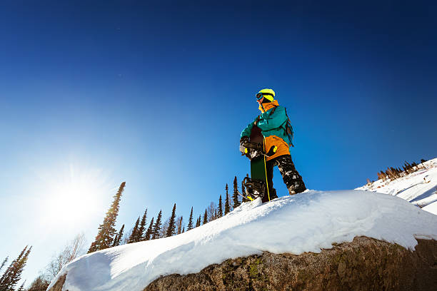 Snowboarder stands and looking far away Snowboarder stands on the big rock keeps snowboard and looking far away. Sheregesh resort, Siberia, Russia Sheregesh stock pictures, royalty-free photos & images