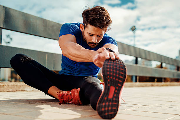 Stretching out Young male jogger athlete training and doing workout outdoors in city cooling down stock pictures, royalty-free photos & images