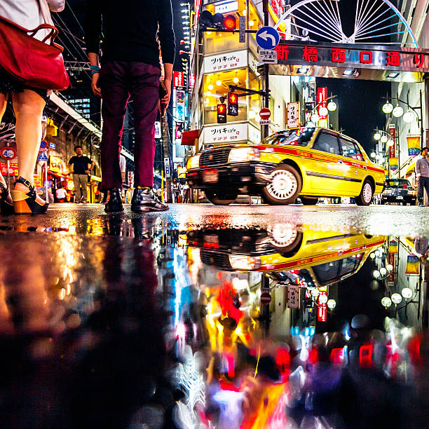 City reflections, Shimbashi, Tokyo. Tokyo, Japan - May 18, 2015: Man and woman waiting to cross the street in Shimbashi business district, just near the train station there is entertainment and nightlife area. Low angle view, reflected in puddle. low angle street japan stock pictures, royalty-free photos & images