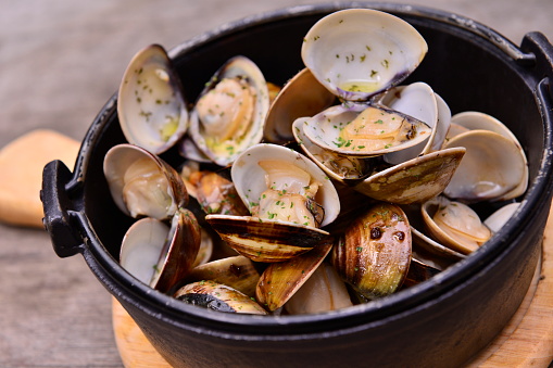 Garlic white wine clam in black pot on wooden tray in asian restaurant