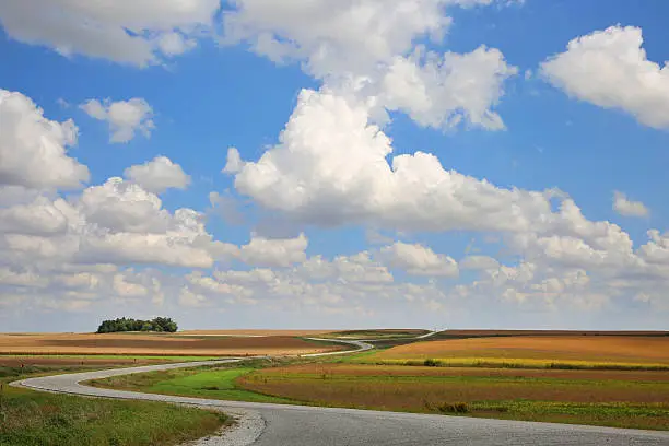 Prairie landscape with beautiful cumulus clouds and blue sky with cloud shadows and long, winding road. Nebraska, September.