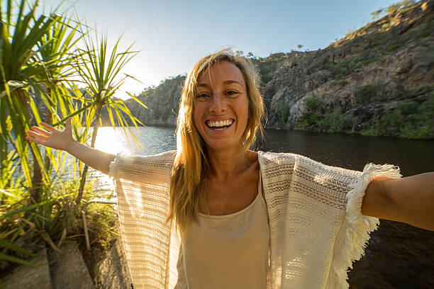 une femme caucasienne prend un portrait selfie au bord du lac au lever du soleil - northern territory flash photos et images de collection