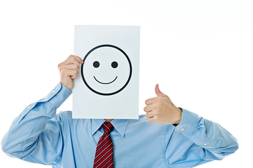 Businessman holding paper with smiley face against white background.