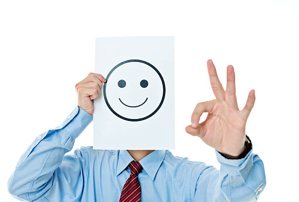 Businessman holding paper with smiley face against white background.