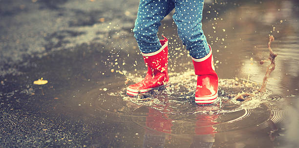 nogi dziecka w czerwonych gumowych butach skaczących w kałużach - red mud zdjęcia i obrazy z banku zdjęć