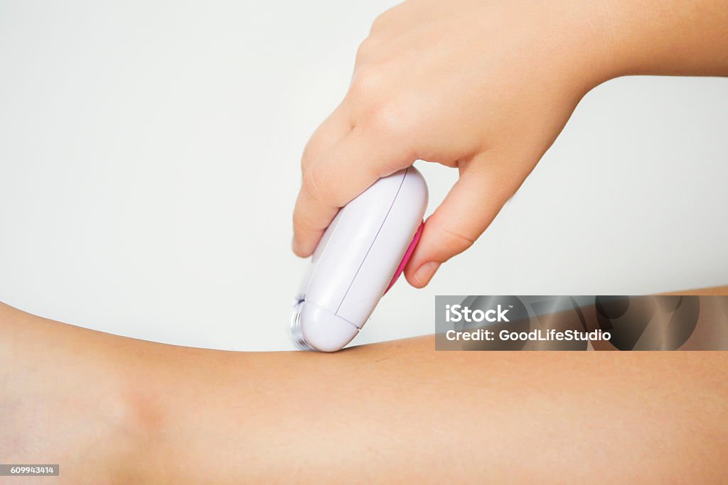 Woman shaving her legs Unrecognizable Caucasian young woman using epilator to shave her legs. Adult Stock Photo
