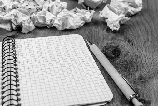 Conceptual image with a spiral notebook on wooden desk surrounded by crumpled drafts and a pen