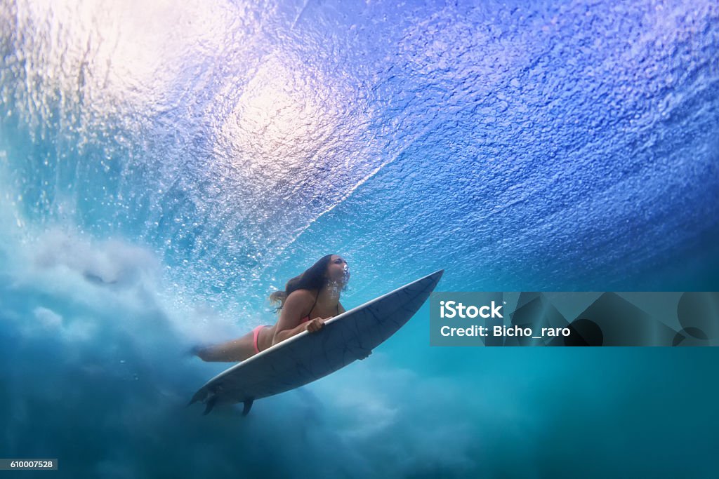 Beautiful surfer girl diving under water with surf board Sportive girl in bikini in action. Surfer with surf board dive underwater under breaking ocean wave. Healthy lifestyle. Water sport, swim and extreme surfing in adventure camp on summer beach vacation Surfing Stock Photo