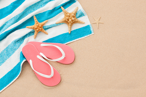 Blue and white striped towel, pink flip-flops and 3 starfishes on beach sand background. Summer beach concept.