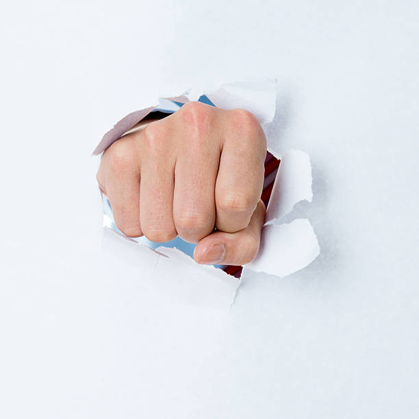istock Man's fist punching through white paper 610012612