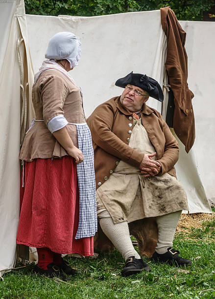 Quiet interlude in a living-history military camp Wheaton, Illinois, USA - September 10, 2016: A man and a woman in period costumes have a discussion by tents in a military encampment at a reenactment of the American Revolutionary War (1775-1783). reenactment stock pictures, royalty-free photos & images