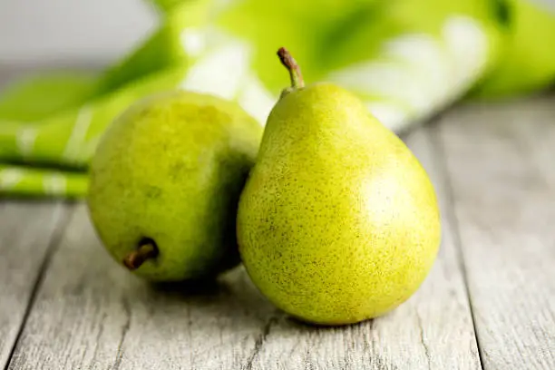 Two Anjou pears sitting on a wooden table with a green tablecloth in the background
