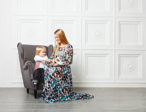 Portrait of the beautiful blond mother with little daughter in armchair